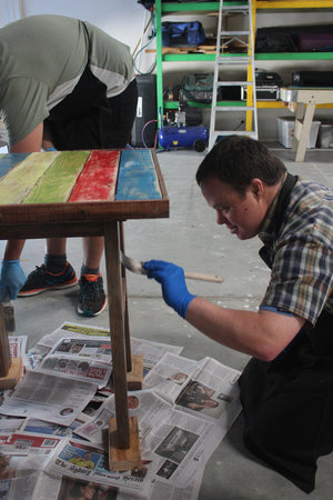 FIRST Service member painting a woodwork project ready for sale in the FIRST store.