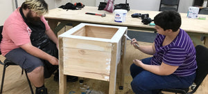 FIRST Service members painting a garden planter box made in our woodwork room to be sold in our store.